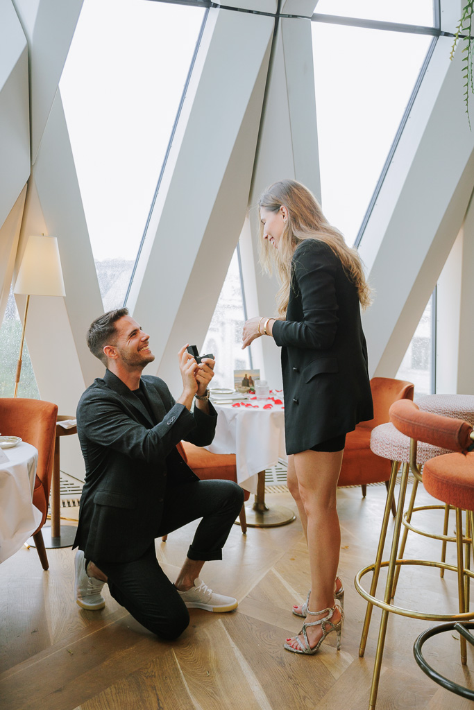 Charming man on his knee proposing to his gorgeous girlfriend at restaurant Chez Bernard in Vienna
