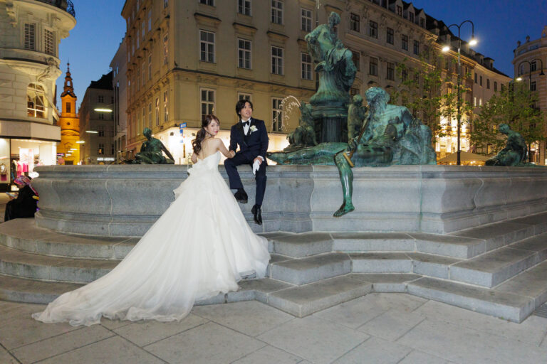 Asian newlyweds posing for a night photo at Neuer Markt square in Vienna, Austria.